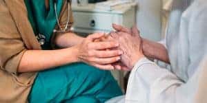 young healthcare worker's hands holding elderly patient's hands