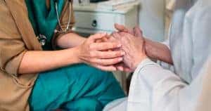 young healthcare worker's hands holding elderly patient's hands
