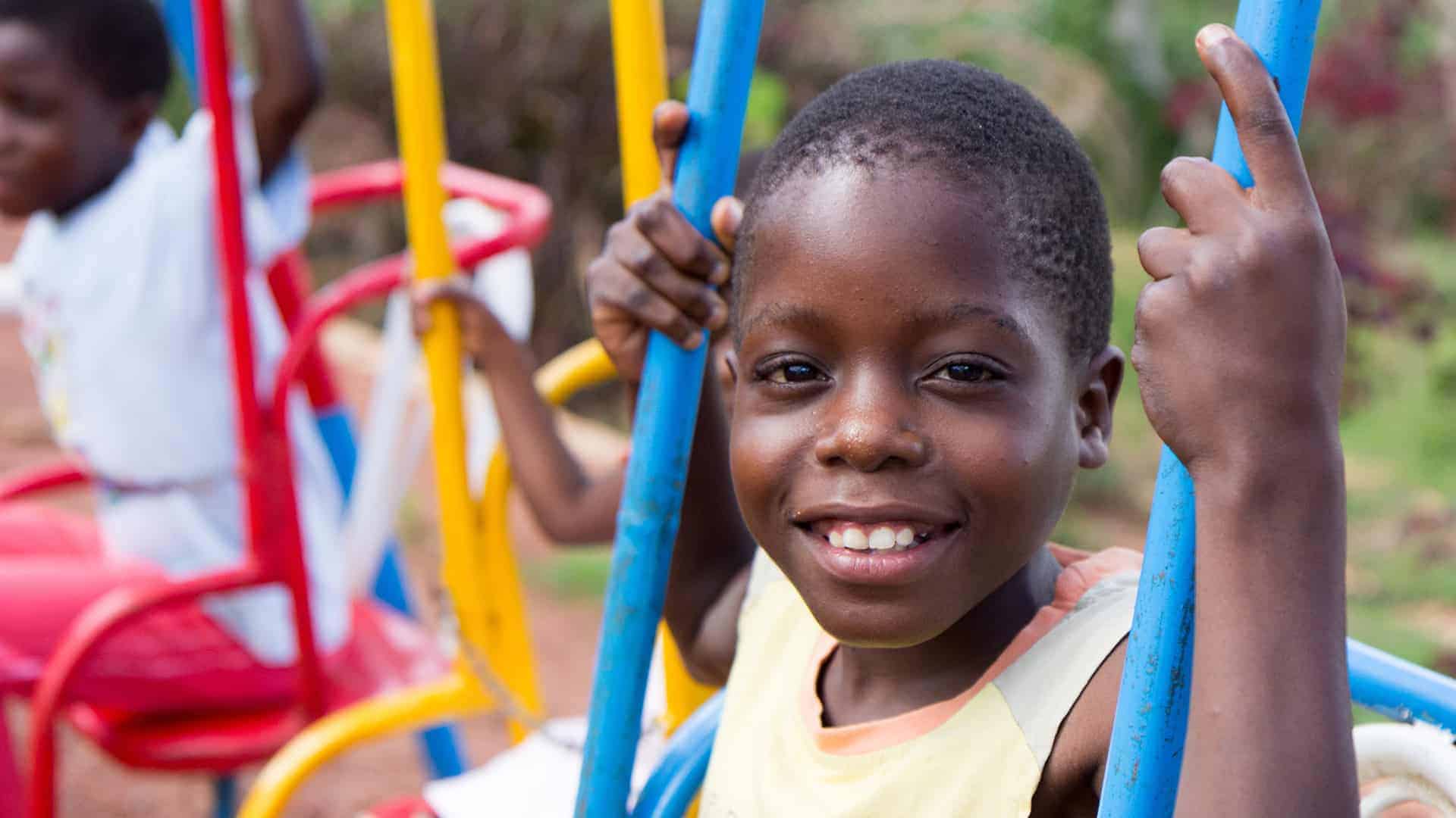 A smiling 13-year old Ugandan boy swinging on a colorful swing