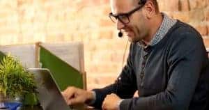 A man wearing his headphone and working on the laptop with a gentle smile on his face