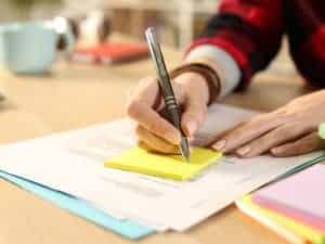 Women writing on a yellow sticky note with a cup in the back which is blurred