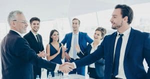 Group of people in formal attire congratulating/applauding a man for his team promotion