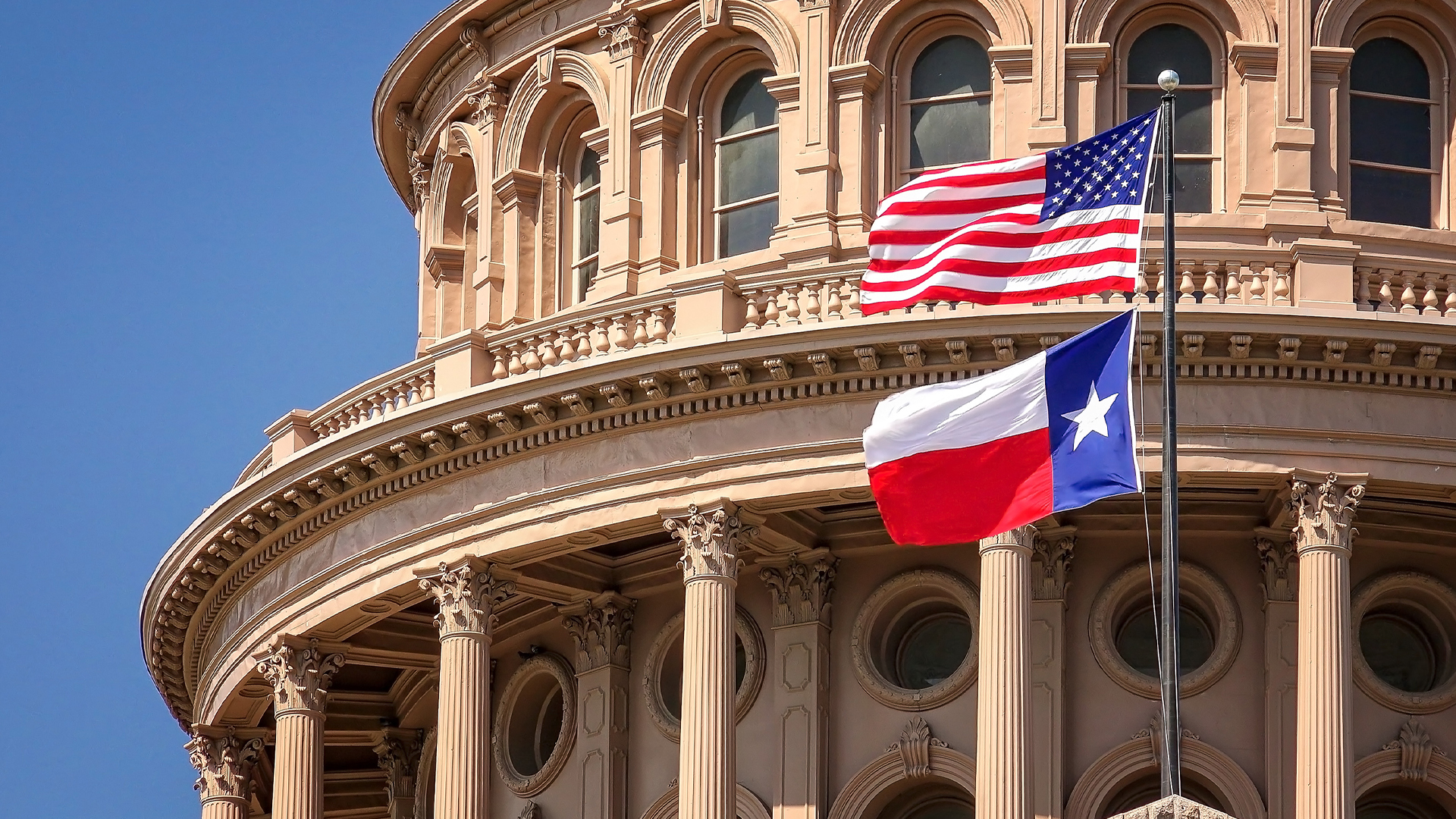 American and Texas state flags flying on the dome of the Texas State Capitol building in Austin