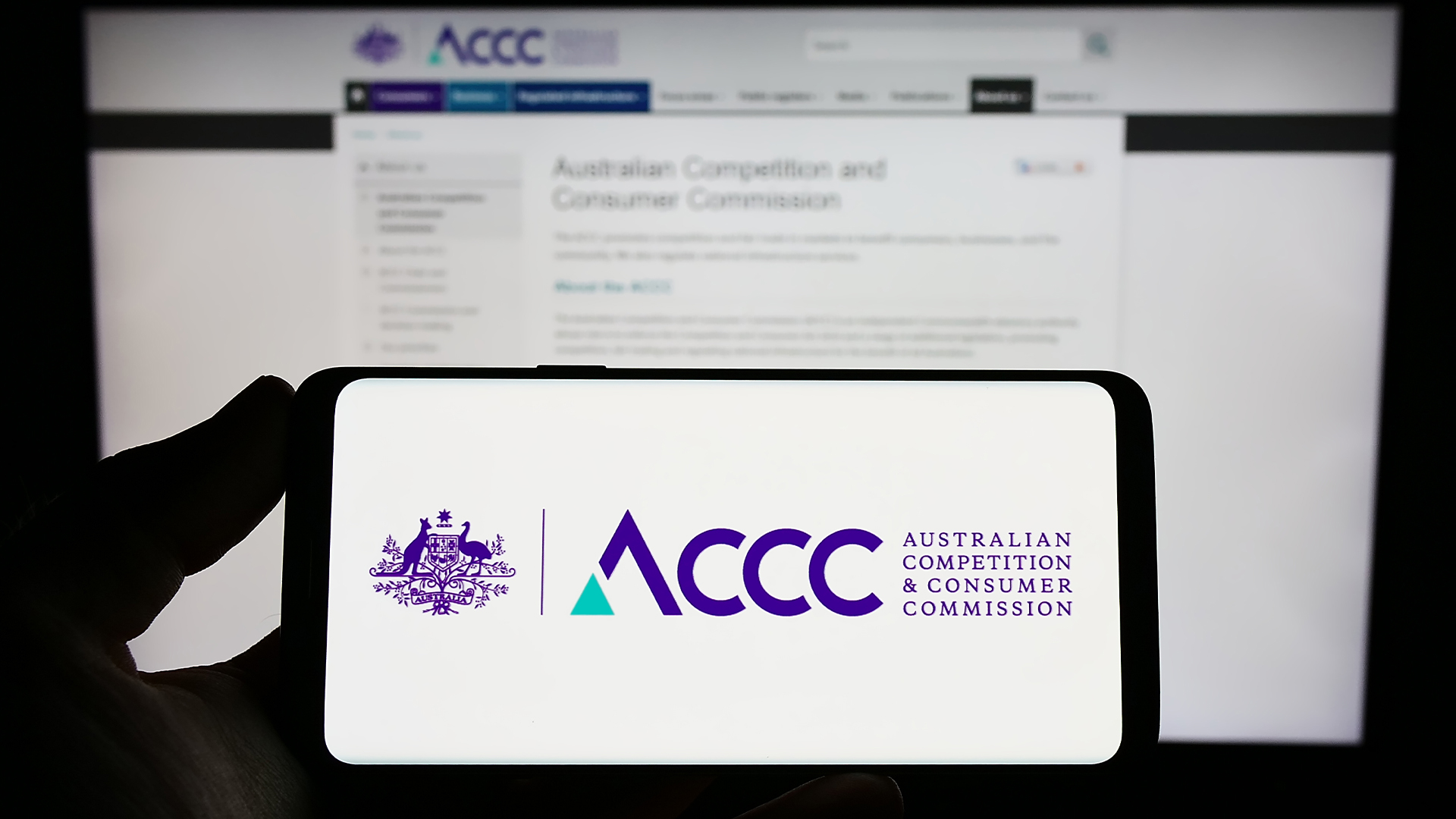 Person holding smartphone with logo of Australian Competition and Consumer Commission on screen in front of website